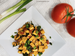 Tofu on plate with green onions and tomatoes. 