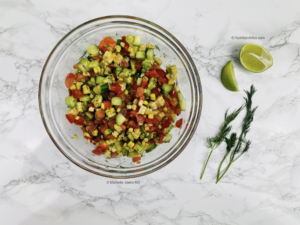 Corn, cucumber, peppers and tomatoes in bowl with lime juice and dill on the side.